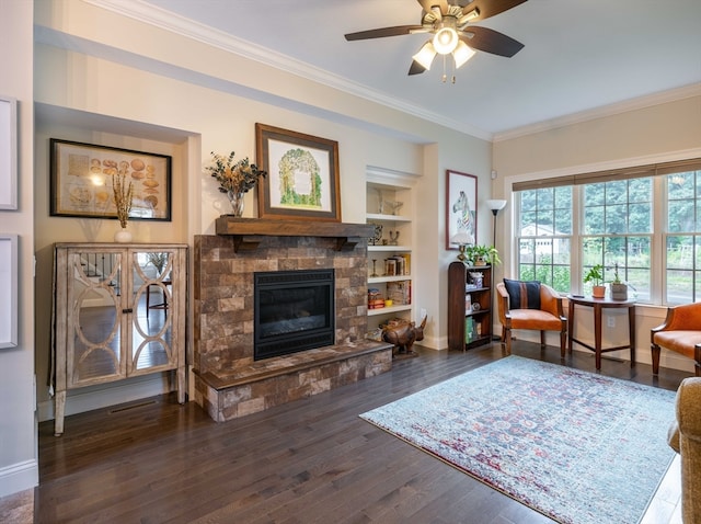 living room with ceiling fan, built in features, dark hardwood / wood-style floors, crown molding, and a fireplace