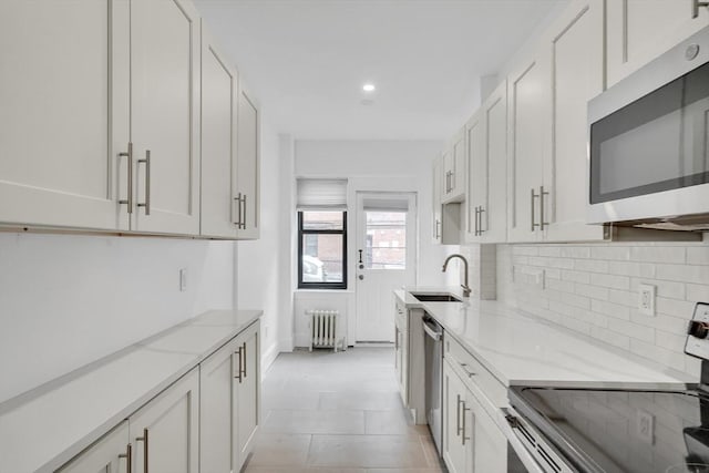 kitchen with radiator heating unit, sink, white cabinets, stainless steel appliances, and light stone countertops