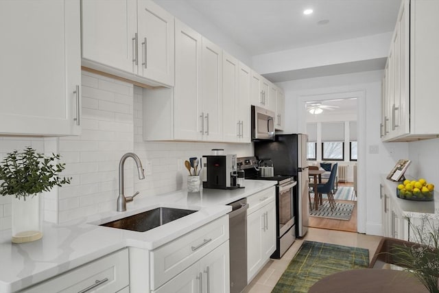 kitchen featuring appliances with stainless steel finishes, white cabinetry, sink, light tile patterned floors, and light stone countertops