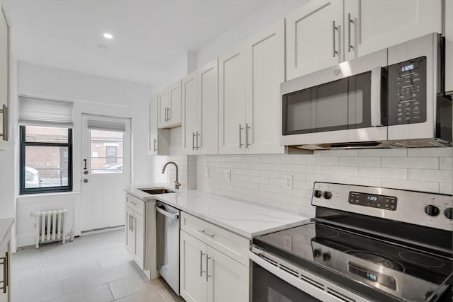 kitchen with sink, white cabinetry, appliances with stainless steel finishes, radiator heating unit, and backsplash