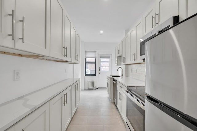 kitchen with sink, white cabinetry, radiator heating unit, stainless steel appliances, and light stone countertops