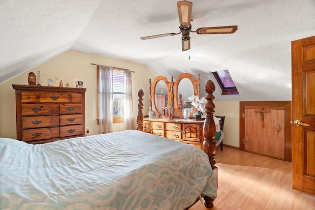 bedroom with a textured ceiling, light hardwood / wood-style flooring, lofted ceiling with skylight, and ceiling fan