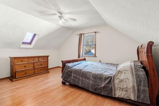 bedroom with vaulted ceiling with skylight, ceiling fan, light wood-type flooring, and a textured ceiling