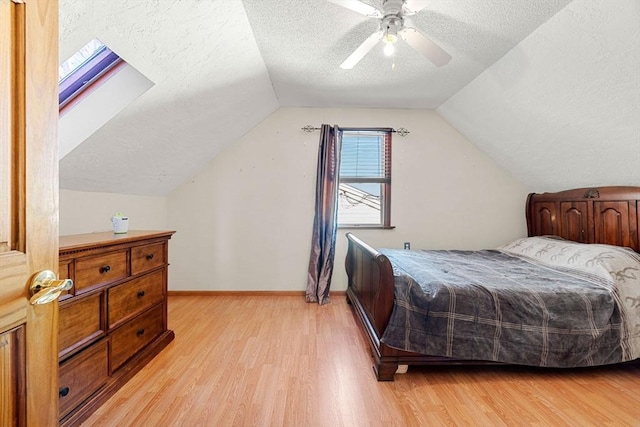 bedroom featuring a textured ceiling, light wood-type flooring, lofted ceiling with skylight, and ceiling fan