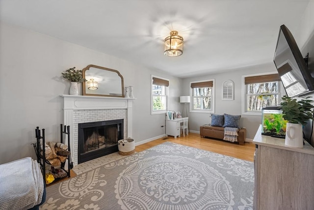 sitting room with a tile fireplace, baseboards, and light wood-style flooring