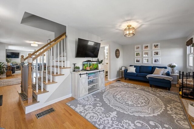 living area with baseboards, stairs, visible vents, and light wood-style flooring