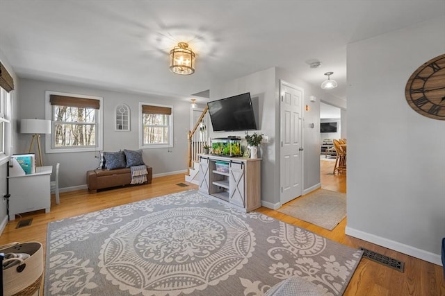 living area with light wood-style floors, baseboards, visible vents, and stairs