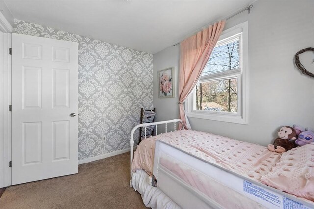 carpeted bedroom with wallpapered walls, an accent wall, and baseboards