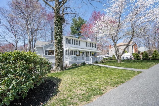 colonial home featuring a chimney, a front yard, and covered porch