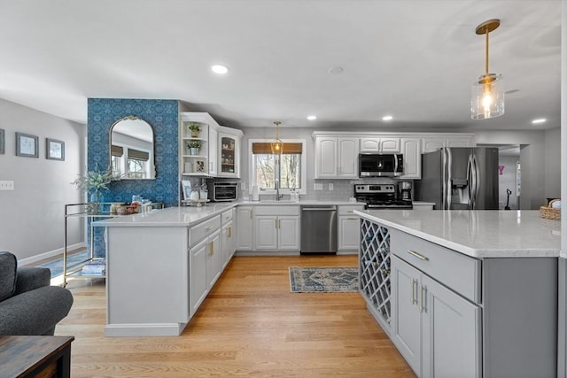 kitchen featuring light wood finished floors, stainless steel appliances, a sink, decorative backsplash, and a peninsula