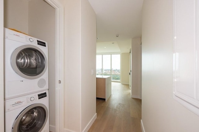 clothes washing area featuring stacked washing maching and dryer and light hardwood / wood-style floors