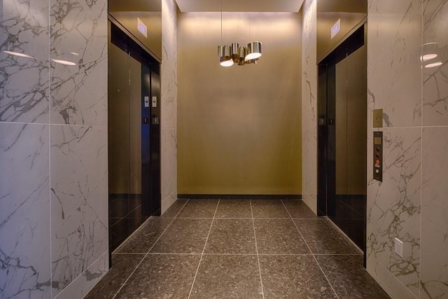 corridor with tile walls, elevator, and an inviting chandelier