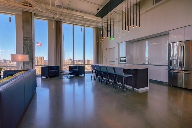 kitchen with white cabinetry, a kitchen breakfast bar, stainless steel fridge with ice dispenser, expansive windows, and a kitchen island