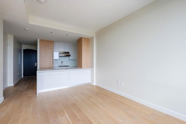 kitchen with white cabinetry, sink, light hardwood / wood-style flooring, kitchen peninsula, and light brown cabinetry