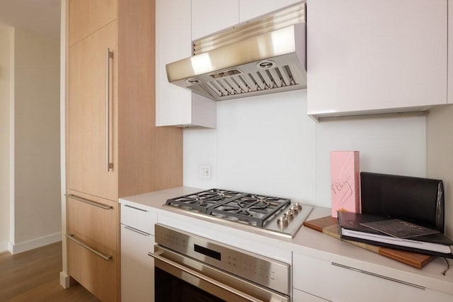 kitchen with wood-type flooring, white cabinetry, stainless steel appliances, and range hood