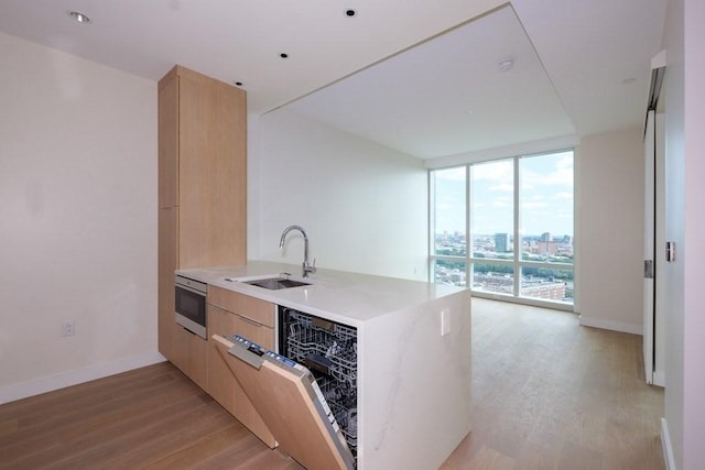 kitchen featuring sink, light brown cabinetry, light hardwood / wood-style floors, a wall of windows, and kitchen peninsula