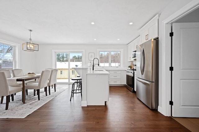 kitchen with a kitchen island with sink, white cabinetry, decorative light fixtures, and appliances with stainless steel finishes