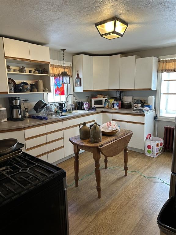 kitchen with light wood-type flooring, radiator, pendant lighting, black gas range, and white cabinets