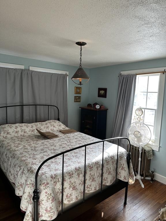 bedroom featuring wood-type flooring, radiator heating unit, and a textured ceiling