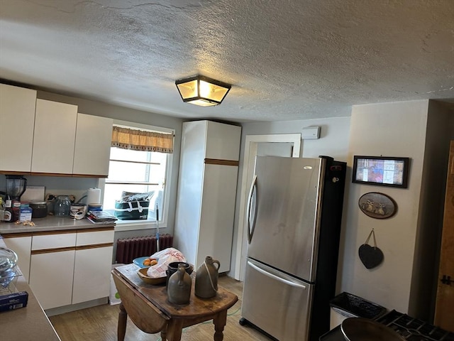 kitchen with white cabinetry, a textured ceiling, stainless steel refrigerator, radiator heating unit, and light hardwood / wood-style floors