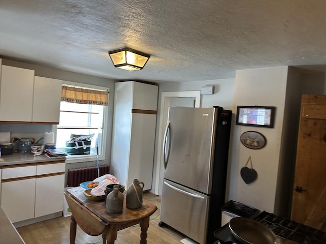 kitchen featuring white cabinetry, light hardwood / wood-style flooring, a textured ceiling, stainless steel refrigerator, and radiator