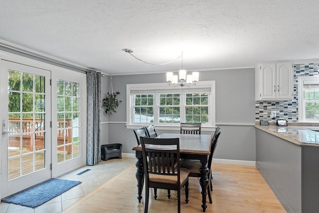 dining room featuring a chandelier, plenty of natural light, a textured ceiling, ornamental molding, and light wood-style floors