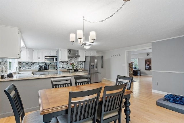 dining area with a chandelier, light wood-style floors, plenty of natural light, baseboards, and a textured ceiling