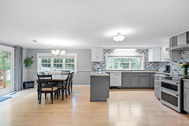 kitchen featuring range with two ovens, gray cabinets, white dishwasher, a chandelier, and healthy amount of natural light