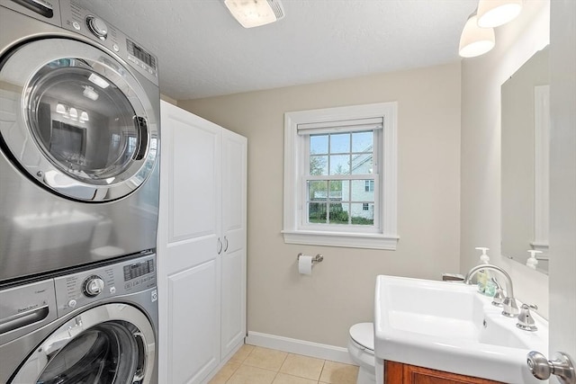 bathroom with stacked washing machine and dryer, baseboards, tile patterned floors, toilet, and vanity