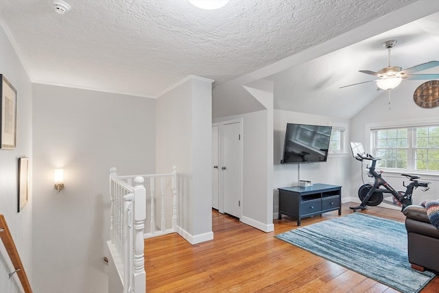 workout area with light wood-style flooring, ceiling fan, baseboards, lofted ceiling, and a textured ceiling