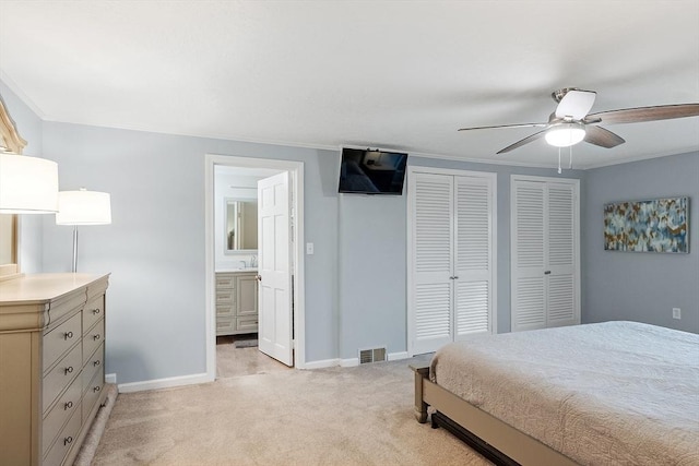 bedroom featuring light carpet, baseboards, a sink, two closets, and ensuite bath