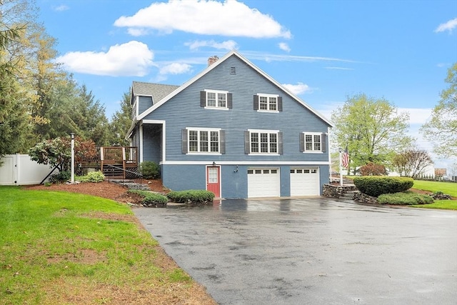 view of side of home with driveway, a garage, a chimney, a wooden deck, and a lawn