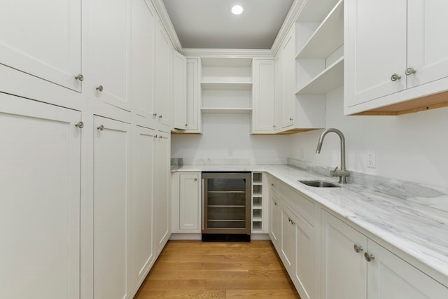 kitchen featuring light wood-type flooring, wine cooler, white cabinetry, light stone counters, and sink