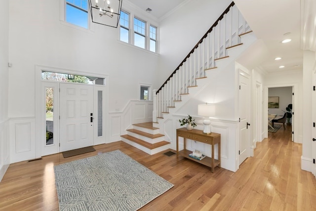 entryway featuring crown molding, a towering ceiling, light hardwood / wood-style flooring, and an inviting chandelier