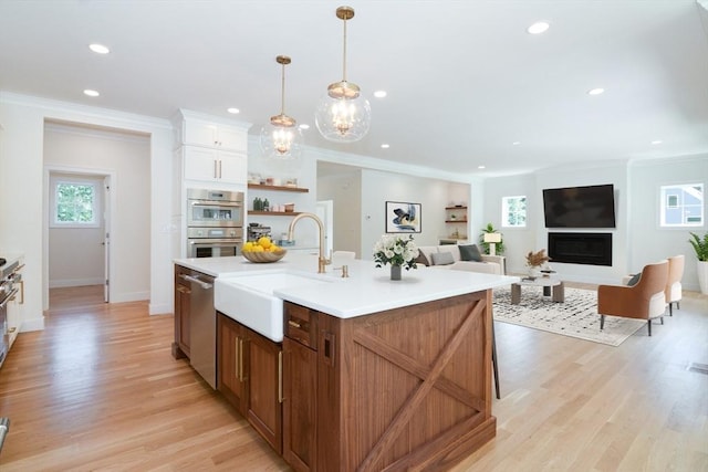 kitchen featuring appliances with stainless steel finishes, light wood-type flooring, sink, hanging light fixtures, and an island with sink