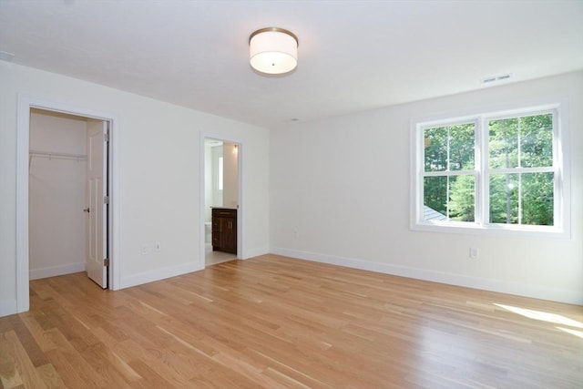 unfurnished bedroom with a closet, light hardwood / wood-style floors, ensuite bath, and a spacious closet