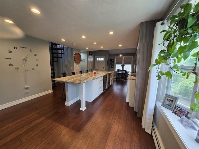 1559 Bay St Unit 53, Taunton, MA 02780 - kitchen featuring a breakfast bar, white cabinetry, baseboards, dark wood-style flooring, and light stone countertops