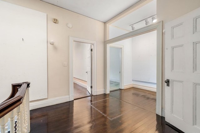 corridor with track lighting, dark wood finished floors, and baseboards