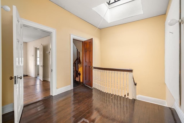 empty room featuring dark wood-style floors, a skylight, and baseboards