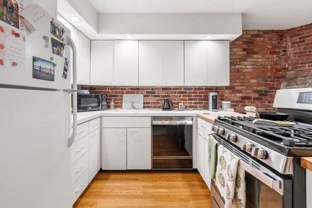 kitchen featuring brick wall, light wood-style floors, white cabinets, light countertops, and black appliances