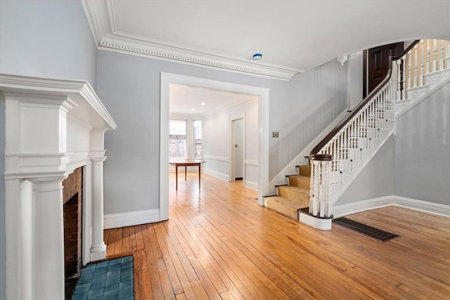 interior space featuring baseboards, wood finished floors, stairs, crown molding, and a fireplace