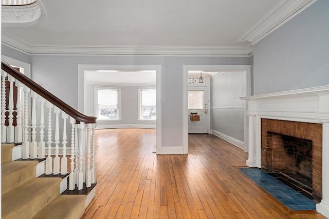 unfurnished living room with stairs, a fireplace, wood finished floors, and crown molding