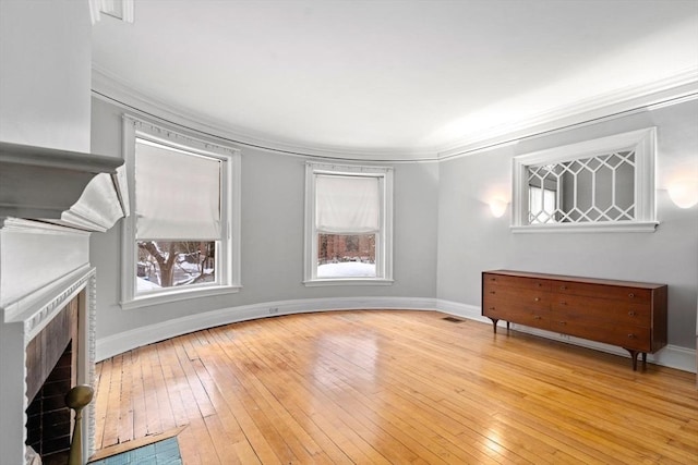 living area featuring a brick fireplace, baseboards, light wood-style floors, and ornamental molding