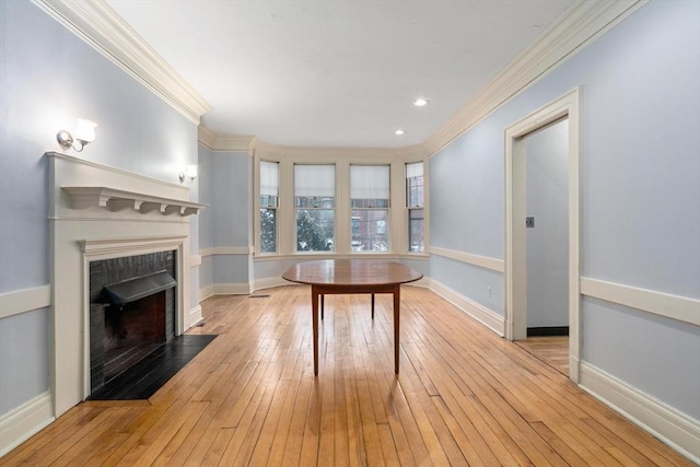 unfurnished dining area with light wood-type flooring, a fireplace with flush hearth, and crown molding