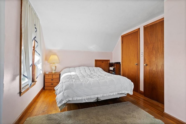 bedroom featuring vaulted ceiling, light wood-type flooring, and multiple closets