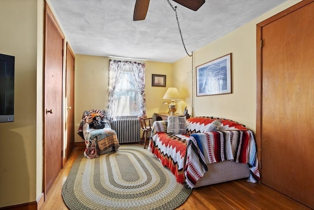 living area featuring hardwood / wood-style floors, ceiling fan, radiator heating unit, and a textured ceiling