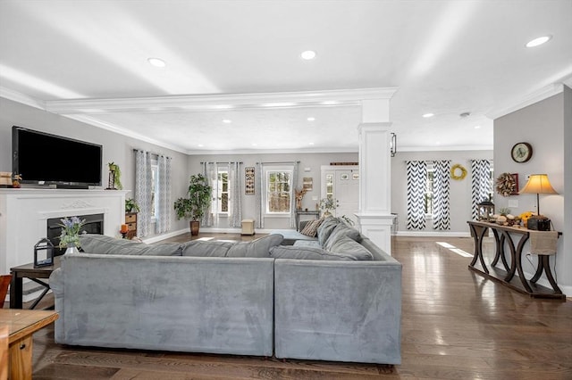 living area featuring dark wood-style flooring, crown molding, a fireplace, recessed lighting, and ornate columns