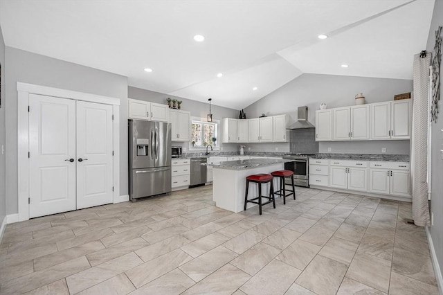 kitchen with a center island, a breakfast bar area, hanging light fixtures, appliances with stainless steel finishes, and wall chimney exhaust hood