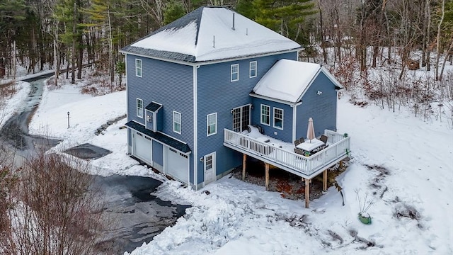 snow covered property featuring an attached garage and a wooden deck