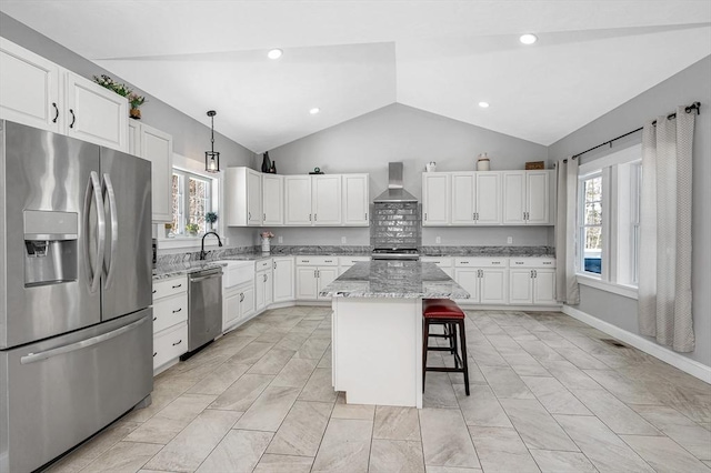 kitchen featuring pendant lighting, wall chimney exhaust hood, stainless steel appliances, a kitchen island, and a kitchen breakfast bar